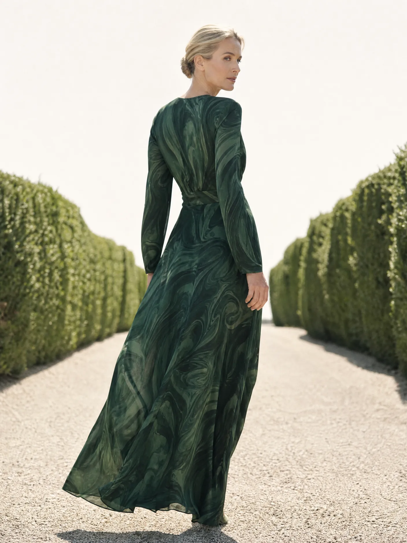 Illustration: a model in a long green swirl-print dress, walking a garden path