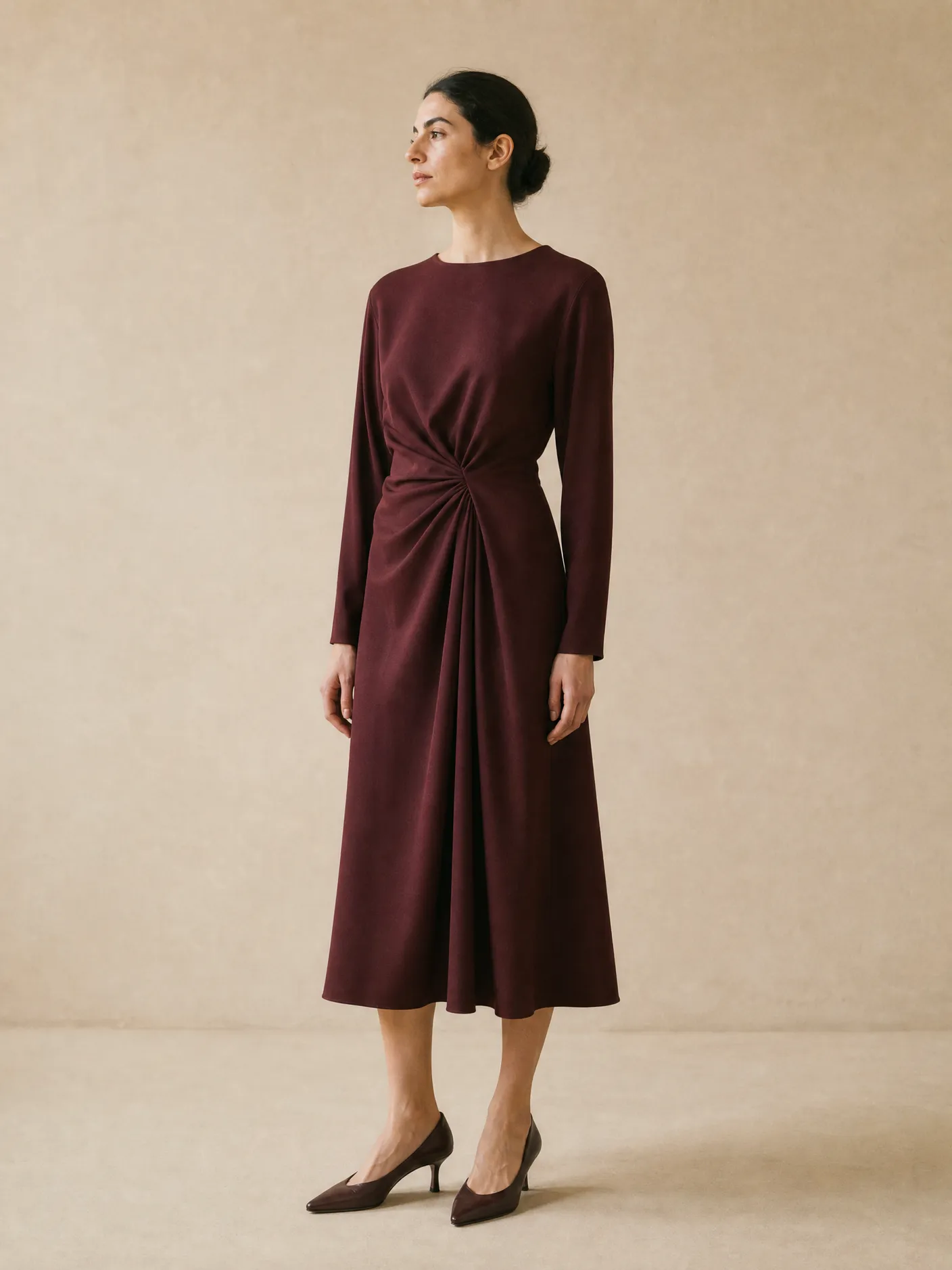 Illustration: a model in a plain burgundy long-sleeved midi dress with a gathered waist, in a studio