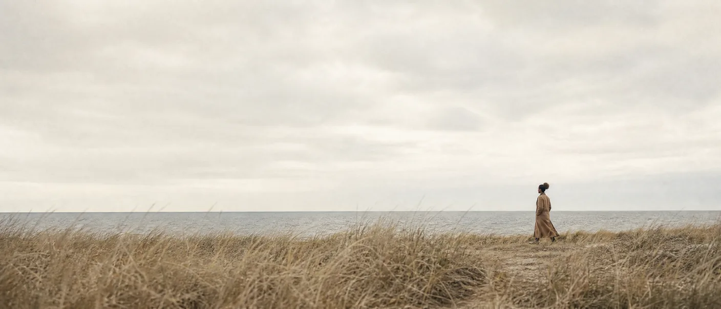 Illustration: a figure in a camel coat on autumn coastal dunes